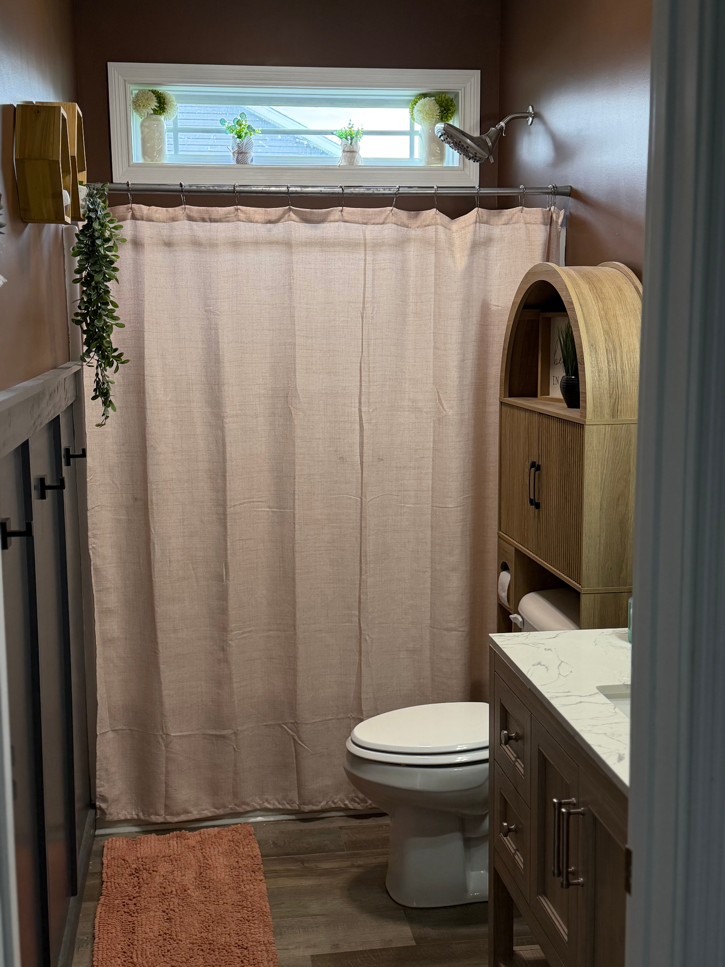 After — Main bathroom transformed with warm mocha walls, wood vanity, marble counter, and arched storage